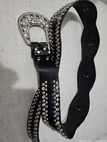 Full view of black decorative belt with silver studs along its length and buckle.