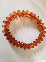 Front view of the stretch bracelet composed of orange faceted beads laid on a white background showing the bead shapes and arrangement.