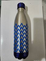 Photo showing a stainless steel water bottle with silver finish and blue geometric pattern all around, blue cap and base visible.