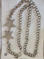 Full view of the chrome finish metal chain belt laid out with two connected star pendants encrusted with rhinestones, lobster claw clasp visible.