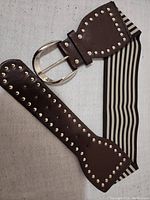 Full view of the brown elastic stretch belt with studded leather ends and silver-tone oval buckle.