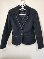 Front view of a women's black blazer showing button closure and gray trim on lapels and pockets.