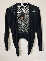 Full view of the black women's cover up top hanging on a hanger showing front and back details.