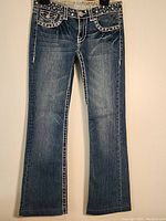 Front view of dark-wash denim jeans featuring decorative stitching and rhinestone accents on front pockets