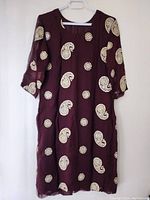 Front view of the maroon dress displaying the jewel and paisley decorations on the fabric and sleeves.