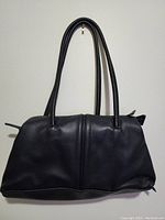 Front view of a black leather handbag with two handles hanging on a white wall.