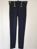 Front full view of black tight pants hanging against white background.