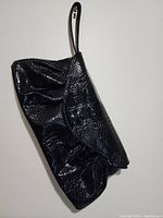 Black purse with glossy faux crocodile texture, showing gathered design and flap closure with wrist strap, lying flat.