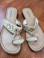 Top view of the pair of cream colored sandals with jeweled upper straps and toe loops showing size and style.