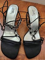 Front view of pair of black satin tie-up dress sandals with rhinestone decorations on straps.