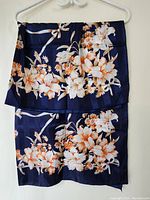 Top view of navy blue scarf folded, showing full lily floral print in white and orange on dark navy background.