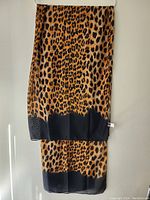 Silk scarf with leopard print and black border hanging vertically showing full length.