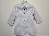 Front view of a white women's button-up shirt with black vertical stripes, collar, and 3/4 sleeves