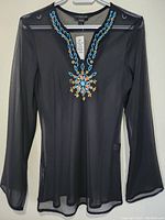Full view of the sheer black silk long-sleeve top hanging on a hanger showing front design and shape.