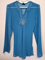 Front view of turquoise silk women's top with embroidered decorative design on neckline and center.