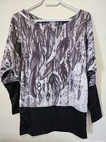 Full front view of women's top with feather and bead print on upper part and black bottom hem and sleeve cuffs.