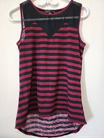 Full view of the sleeveless top hanging on a hanger showing the horizontal black and maroon stripes and curved hemline.