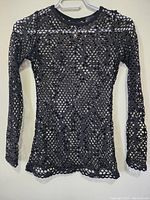 Front view of the women's long sleeve black grey mesh top hanging on a clear hanger showing full length and mesh detail.