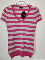 Full view of La VOCA women's top hanging on white hanger showing front, pink and silver horizontal stripes, V-neck, short sleeves, ribbed hem.
