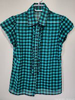 Front view of women's blue and black checkered short sleeve top with ruffle detail on button placket.