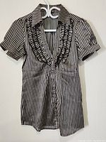 Front view of the black and white vertical striped women's top showing short puff sleeves and button-up front with ruffle detailing.
