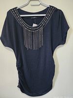 Front view of black women's top with decorative beaded neckline and chain fringe hanging from neckline.
