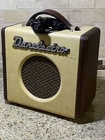 Front view of the Danelectro Dirty Thirty amplifier showing its cream and brown leather case, speaker grille, and handle with power cord on top.