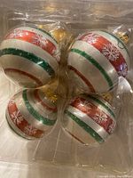 Four Christmas ornaments with red, green, and white stripes and white snowflakes, packaged in a clear plastic container.