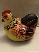 Full side view of a vintage tin hen toy showing its colorful and detailed painted feather pattern and molded red comb on top.