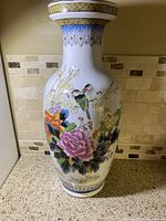 Full view of the tall decorative porcelain vase with floral and bird artwork on a countertop
