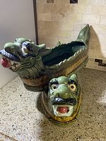 First dragon with head raised showing detailed face with open mouth and red tongue, hollow body planter, green and gold glaze