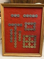 Front view of vintage coin collection displayed in wooden frame with red fabric backing.