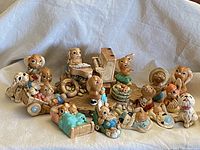 Group of 18 Pendelfin bunny and dog figurines arranged together on a white cloth, showing variety of pieces including bunnies in clothing and a piano on a wooden base.