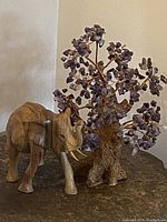 Photo of wooden elephant statue and amethyst gemstone tree together on a stone surface, showing front view of both items