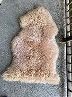 Full view of the beige vintage genuine sheepskin fur rug laid flat on a grey concrete surface showing thick, plush fur texture.
