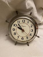 Front view of vintage Ingraham chrome kitchen clock showing round dial, black numerals, red second hand, and chrome ship wheel frame.