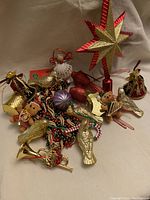 Full view of assorted vintage Christmas ornaments including bird ornaments, garlands, teddy bear figurine, angel, hearts, and bell shaped pieces scattered on white fabric.
