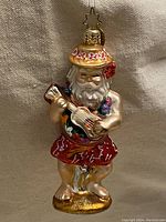 Full view of the Christopher Radko 2001 Don Ho-ho-ho Santa Christmas ornament, showing Santa with a straw hat, red floral skirt, and playing a guitar decorated with flowers.