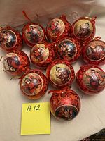 Twelve vintage Victorian style gold paper mache Christmas baubles arranged on white background. Each ball has a detailed festive illustration and hanging loop.