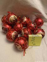 Set of 12 red and gold Victorian style paper mache Christmas ornaments scattered on a white background.