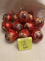 Group photo of 12 vintage paper mache Christmas baubles with Victorian style illustrations including Santa Claus and children. Red and gold color scheme on glossy spherical ornaments with hanging loops and some ribbons.
