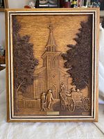 Full view of framed bas-relief carved wood artwork depicting church scene with people and horse carriage.