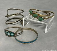 Five vintage bracelets including two gold-tone mother of pearl stone bangles, one silver-tone bangle with blue enamel, a snake-shaped bracelet, and a silver-tone coiled bangle with diamond pattern details.
