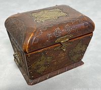 Front view of the small wooden chest showing brass star-shaped decorative plate on the top and brass latch on the front.