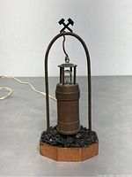 Full view of the antique miner lantern lamp suspended from a metal arch with a wooden base and simulated coal detail. Shows condition and structure.