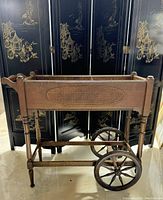 Side view of the antique wooden cart planter showing the cane pattern oval insert and large wooden wheels with hexagonal spokes.