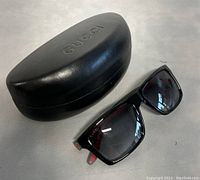 Front view of sunglasses next to black GUCCI hard case