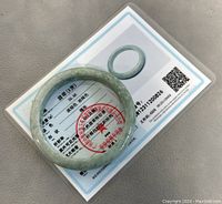 Photo of the jade bangle resting on a certification card with text and a red stamp.