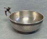 Photo showing side view of the silver cup or bowl with detailed bird figurine on the handle and decorative border around the rim.
