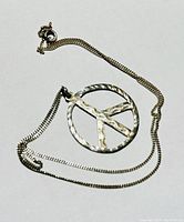 Photo of the complete necklace laid flat, showing the peace sign pendant and chain.